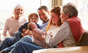 Mehrgenerationen-Familie sitzt auf dem Sofa mit neugeborenem Baby lächelt