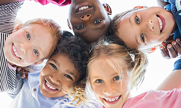Closeup face of happy multiethnic children embracing each other and smiling at camera. Team of smiling kids embracing together in a circle. Portrait of young boy and pretty girls looking at camera
