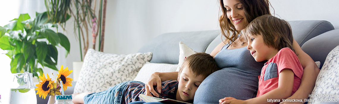 Junge schwangere Frau, ihren beiden Jungen zu Hause ein Buch vorlesen, Früchte essen, umarmen und lachen